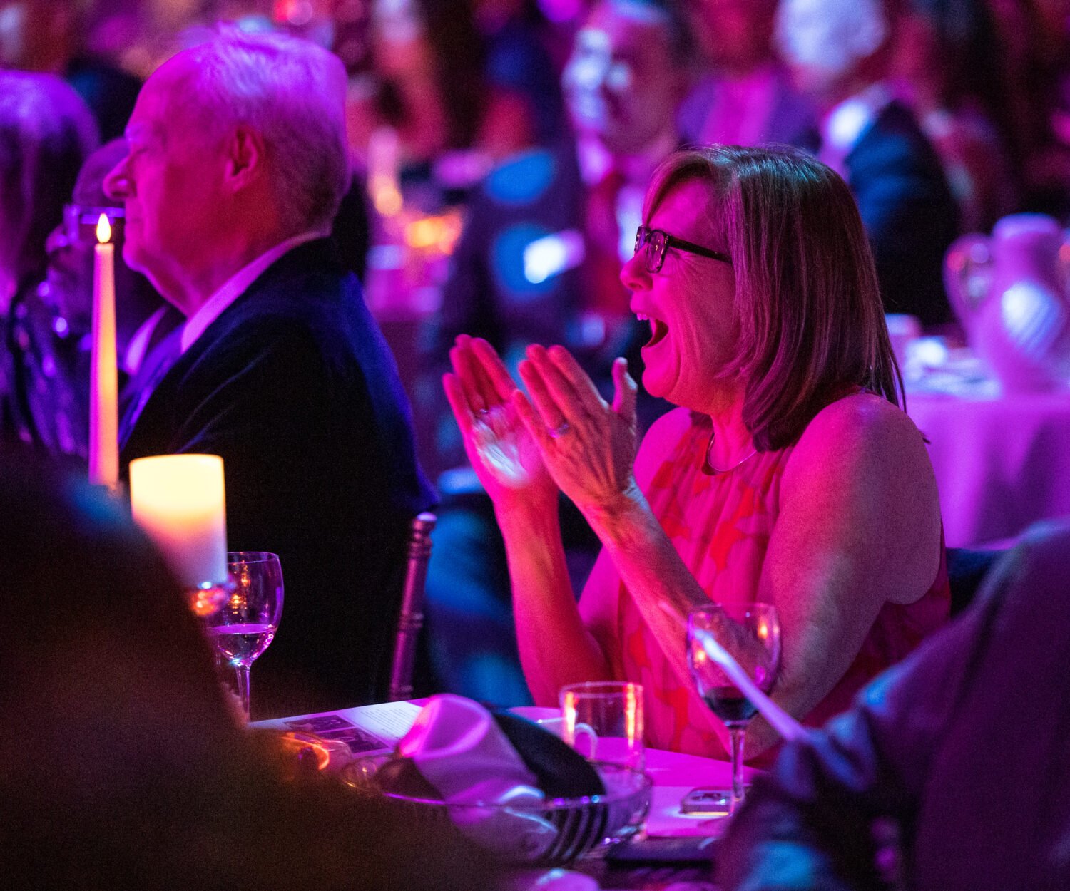 Woman in pink lighting clapping and smiling in delight.